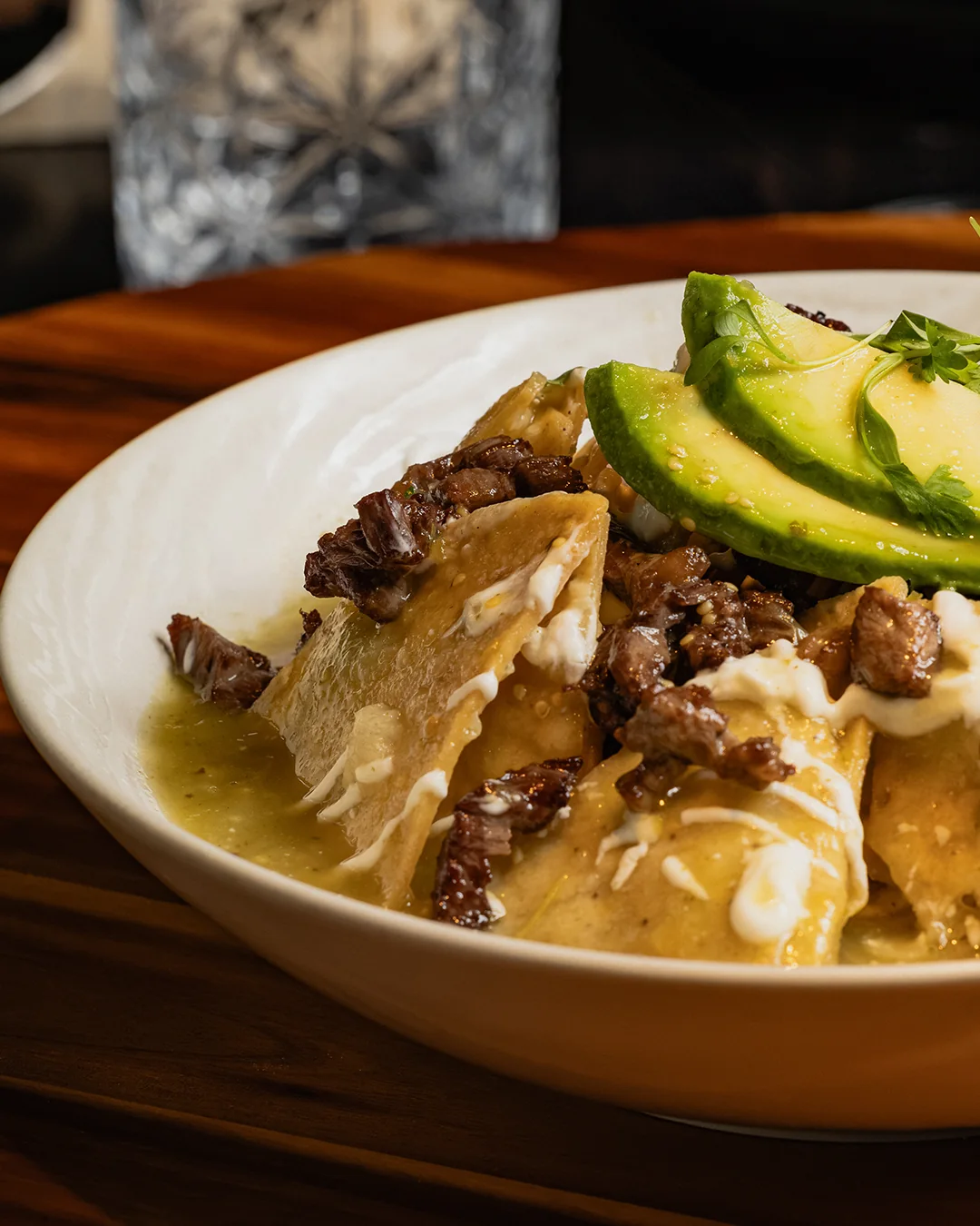 Sauced tortilla chips topped with meat, crema and fresh avocado at Origen Gilbert