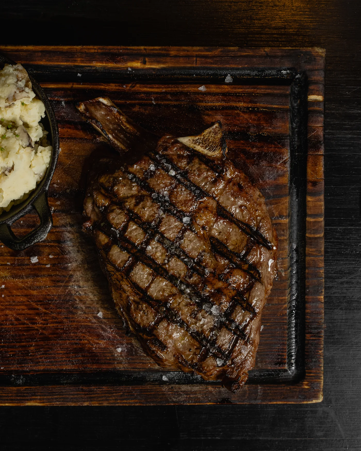 A grilled steak served on a dark wooden board at Origen Gilbert.