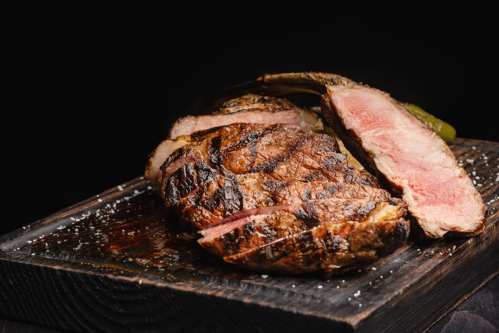 Origen’s grilled ribeye, sliced to show its pink center, on a wooden board